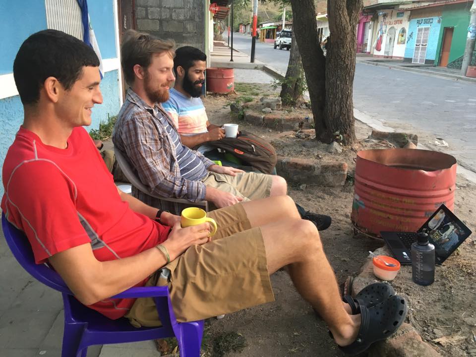 Three men sit outside and watch YouTube videos on an ipad